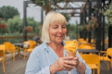 Happy smiling senior woman dressed in stylish clothes eating ice cream in the city summer outdoors cafe interior. High quality photo