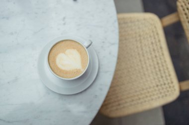 Beyaz kahve fincanını yakın plan çek, kafenin penceresinin yanında kalp şeklinde latte sanatı olan sıcak kapuçino. Yüksek kalite fotoğraf