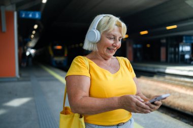 İstasyonda treni bekleyen ve akıllı telefon kullanan mutlu 50 'li yaşlarda bir kadın. Yüksek kalite fotoğraf