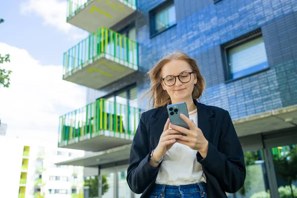 Smiling businesswoman using her phone outdoors. Small business entrepreneur looking at her mobile phone and smiling while communicating with her office colleagues. High quality photo