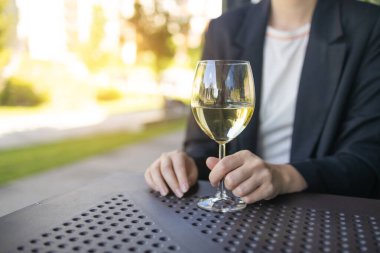 Restoranda bir kadeh beyaz şarap içen zarif sarışın bayan. Estetik beyaz şarap ya da bulanık şehir kafesi arka planında su. Yüksek kalite fotoğraf