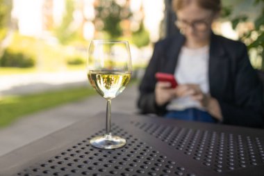 Restoranda bir kadeh beyaz şarap içen zarif sarışın bayan. Estetik beyaz şarap ya da bulanık şehir kafesi arka planında su. Yüksek kalite fotoğraf