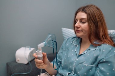 Evde astım spreyi kullanarak nefes aldırmak için yüzüne nebulizör maskesi takan genç hasta kadının portresi. Tıbbi inhaler acil durum ekipmanı, astım krizi. Yüksek kalite fotoğraf