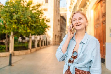Gülümseyen genç bir kadın ya da genç bir kız şehir caddesinde akıllı telefondan arıyor. Teknoloji, iletişim, yaşam tarzı ve insan kavramı. Yüksek kalite fotoğraf