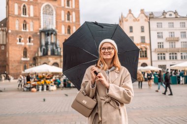 Yağmurlu bir günde, bir şemsiyenin altında şık bir palto giymiş ve eski bir kasabada nefes alan mutlu bir kadının portresi. Yüksek kalite fotoğraf