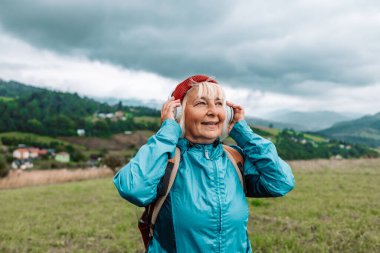 Açık havada müzik dinleyen ve doğa güzelliğinden esinlenerek manzaraya hayran olan mutlu, aktif, yaşlı turist kadın. Yüksek kalite fotoğraf