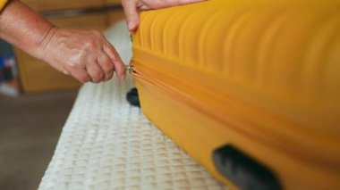 Yatak odasındaki sarı valiz çantasının fermuarını çekerken ellerinizi kapatın. Tatil seyahati için bavul hazırlıyorum. Yüksek kaliteli FullHD görüntüler