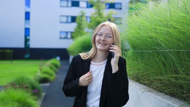 企業の女性の肖像画は オフィスビルに歩いている間 電話に答えます ビジネスマンが誰かを呼んでいる 高品質で — ストック動画