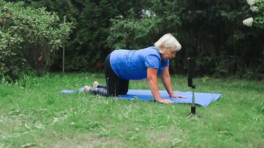 50 'li yaşlarda beyaz bir kadın spor minderinde yoga yapıyor. Parkta ya da ormanda dijital tabletle ya da kulaklıklarla meditasyona hazırlanıyor. Yüksek