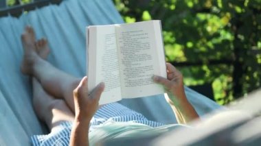Güzel sarışın kadın kitap okuyor ve bahçedeki hamakta dinleniyor. Yüksek kalite 4k görüntü