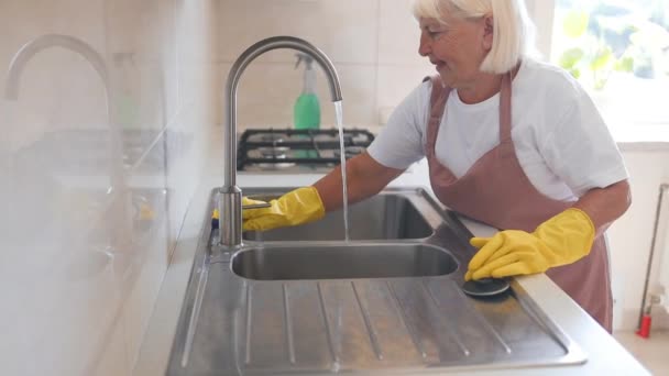 週末の主婦50代女性ハウスキーピング 黄色の保護ゴム手袋でスポンジ付きのキッチンキャビネットを掃除する女性 高品質のフルHd映像 — ストック動画