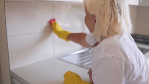 50代のシニア主婦がゴム製手袋を着用し 家庭で台所の表面を拭き取り 家をきちんと保管しています ハッピープロの女性のクリーニング労働者は屋内でほこりをモッピングします 高品質のフルHd映像 — ストック動画