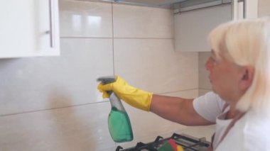 50 'li yaşlarda lastik eldiven takan, evde mutfak yüzeylerini silen, evi düzenli tutan bir ev hanımı. İçerideki tozları silen mutlu profesyonel kadın temizlikçi. Yüksek kaliteli FullHD görüntüler