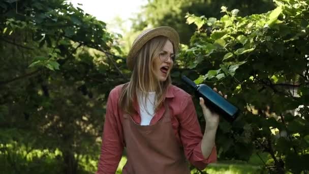 赤ワインダンスのガラスボトルとハッピーな若い女性は 晴れた日にワイナリーの田舎で一日を楽しんでいます 日没前にブドウ畑で赤ワイングラスを試飲する 高品質のフルHd映像 — ストック動画