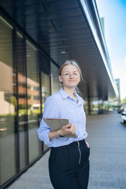 Young elegant professional leader Caucasian woman, female executive retail manager supervisor, small business owner wearing suit holding digital tablet standing outdoor looking at camera, portrait.