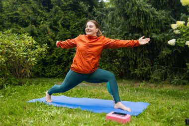 30 'lu yaşlardaki atletik bir kadın yoga minderinde poz veriyor. Spor kıyafetleri giyip parkta ya da ormanda tek başına poz veriyor. Yüksek kalite fotoğraf