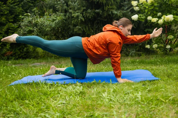 stock image Athletic 30s woman doing poses at yoga mat outdoors dressed in sport clothes alone in the park or forest in nature. High quality photo