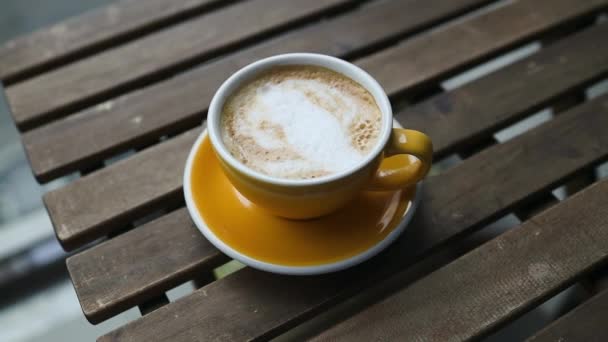 在木制咖啡桌上的一个陶瓷黄色杯子里 可以看到热拿铁咖啡和拿铁艺术的侧面景观 优质Fullhd影片 — 图库视频影像