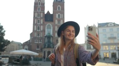 Krakow 'daki eski şehir meydanında elinde cep telefonu olan güzel, şık, beyaz bir kadın selfie ya da video çekimi yapıyor. 