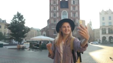 Krakow 'daki eski şehir meydanında elinde cep telefonu olan güzel, şık, beyaz bir kadın selfie ya da video çekimi yapıyor. 