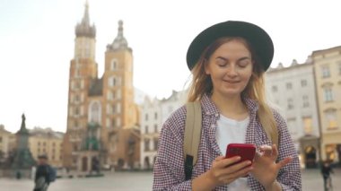 Aziz Mary Bazilikası. Krakow 'daki Pazar Meydanı' nda tek başına seyahat ederken navigasyon uygulamasını telefonla kullanan ve eski şehirde yürüyen sarı sırt çantalı genç beyaz bir kadın. Avrupa 'yı gezmek. Yüksek