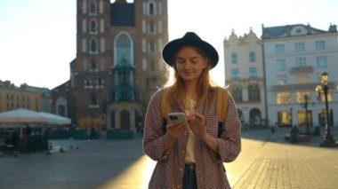 Krakow 'daki eski şehir meydanında elinde cep telefonu olan güzel, şık, beyaz bir kadın selfie ya da video çekimi yapıyor. 
