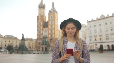 Aziz Mary Bazilikası. Krakow 'daki Pazar Meydanı' nda tek başına seyahat ederken navigasyon uygulamasını telefonla kullanan ve eski şehirde yürüyen sarı sırt çantalı genç beyaz bir kadın. Avrupa 'yı gezmek. Yüksek