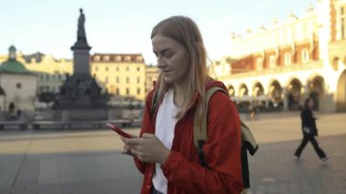 Aziz Mary Bazilikası. Krakow 'daki Pazar Meydanı' nda tek başına seyahat ederken navigasyon uygulamasını telefonla kullanan ve eski şehirde yürüyen sarı sırt çantalı genç beyaz bir kadın. Avrupa 'yı gezmek. Yüksek