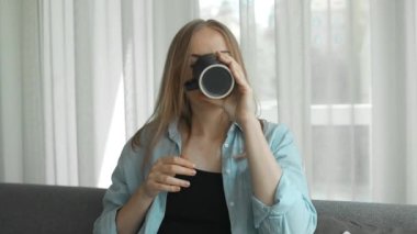 Hoş gülüşü olan, sıcak çay ya da oturma odasında kahve içen yorgun genç bir kadın. Olumlu bir yetişkin kadın evdeki kanepede dinleniyor. Yüksek kaliteli FullHD görüntüler