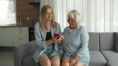 Sevgi dolu bir aile. Anne ve kızı evde telefon kullanarak vakit geçiriyorlar. Büyükannem akıllı telefon ekranına bakıyor, video veya fotoğraf izliyor, evdeki rahat kanepede birlikte oturuyor.