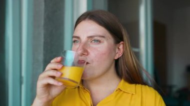Portakal suyu içen mutlu kadın pencereden bakıyor, sağlıklı yemek ve içki konsepti. Yüksek kaliteli FullHD görüntüler