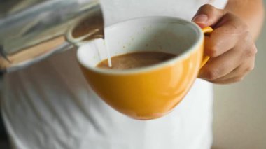 Erkek ellerinin süt dökerken ve taze kapuçino hazırlarken yakın plan görüntüsü, kahve sanatçısı ve hazırlık konsepti, sabah kahvesi. Yüksek kaliteli FullHD görüntüler