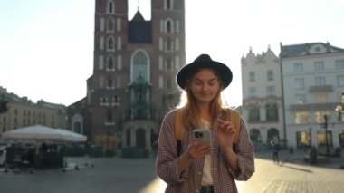 Krakow 'daki eski şehir meydanında elinde cep telefonu olan güzel, şık, beyaz bir kadın selfie ya da video çekimi yapıyor. 