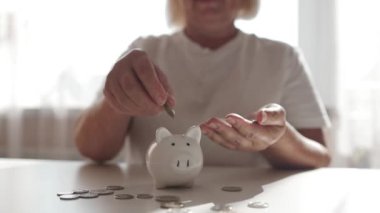 50 'li yaşlardaki yaşlı bir kadın para biriktirmek ve finansal konsept için domuzcuğa para yatırıyor. Yüksek kaliteli FullHD görüntüler