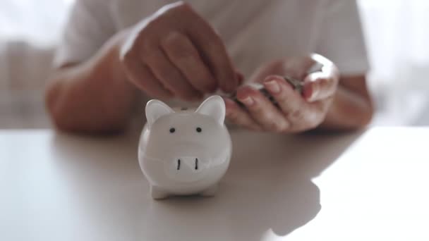 シニア50代の女性は お金の富と金融コンセプトを節約するために お金のコインを豚に渡します 高品質のフルHd映像 ロイヤリティフリーのストック動画