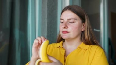 Tatlı, genç, beyaz, aç, 30 'lu yaşlarda muz kaplayan bir kadın. Sabahları mutfak odasında muz yiyen güzel bir kadın. Yüksek kaliteli FullHD görüntüler
