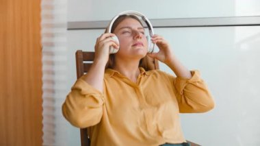 Genç, güzel, beyaz bir kadın terasında oturmuş kulaklık takıyor ve müzik dinliyor.. 