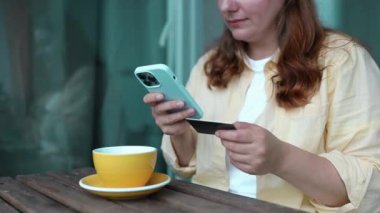 Akıllı telefon ve kredi kartını elinde tutan çekici beyaz kadın mobil bankacılık uygulaması ya da online alışveriş uygulaması kullanıyor. Yüksek kaliteli FullHD görüntüler