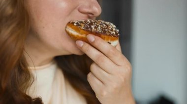 Beyaz kremalı donut yiyen 30 'lu yaşlardaki aç bir kadının portresi. Kız tatlı hamur işlerini kokluyor. Paket servis ederken çörek yemek. Memlekette fast food servisi. Yüksek kaliteli FullHD görüntüler