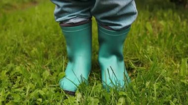 Yeşil çimenlerin üzerinde yürürken lastik siyah botları kapatın. Kirli çiftçiler yeşil çimlerde yürüyen lastik botlar..