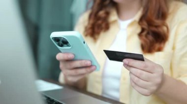 Akıllı telefon ve kredi kartını elinde tutan çekici beyaz kadın mobil bankacılık uygulaması ya da online alışveriş uygulaması kullanıyor. Yüksek kaliteli FullHD görüntüler