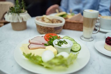 Haşlanmış yumurta, yeşil salata, salatalık ve baldırla sağlıklı bir kahvaltı. Arka planda kahve ve taze mısır gevreği var..