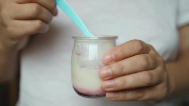 Evde meyve ve yoğurtla sağlıklı kahvaltı eden gülümseyen genç bir kadın. Evde böğürtlenli taze yoğurt yiyen bir kadın. Yüksek kaliteli FullHD görüntüler