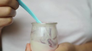 Beyaz kadın evde meyve ve yoğurtla sağlıklı kahvaltı yapıyor. Elinde yoğurt ve yaban mersinli çay kaşığı tutan mutlu doğal kız, yakın plan. Yüksek kaliteli FullHD görüntüler