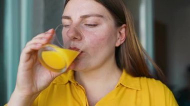 Kadın sarı meyve suyu detoks kokteyli içiyor. Yakından bakınca portakal suyunu bir bardakta tadıyor ve sabahları içkinin tadını çıkarıyor. Fitness ve sağlıklı yaşam tarzı konsepti. Yüksek kalite FullHD