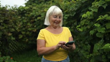 Yaz bahçesinde dinlenirken cep telefonunu ve mesajlarını kullanan orta yaşlı çekici bir kadının portresi.