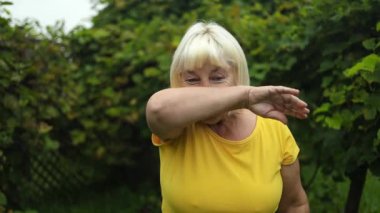 Hastalıklar ve ilaçlar. Alerjisi olan yaşlı bir kadın yaz parkında üşüttüğü için elleriyle burnunu siler. Yüksek kaliteli FullHD görüntüler