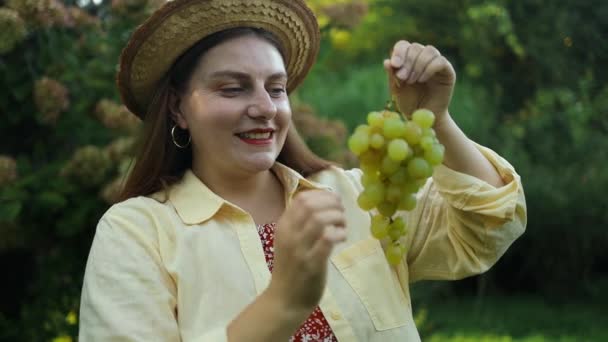 笑顔のコーカサス女性の肖像画は 日没時に屋外で甘い白いブドウの健康的な食べ物を食べています ブドウを食べている若い女性 食べ物 飲み物 ライフスタイルコンセプト — ストック動画