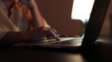 Öğrenci kız ellerinin gece evdeki bir masada oturup dizüstü bilgisayardaki notları karşılaştırması.