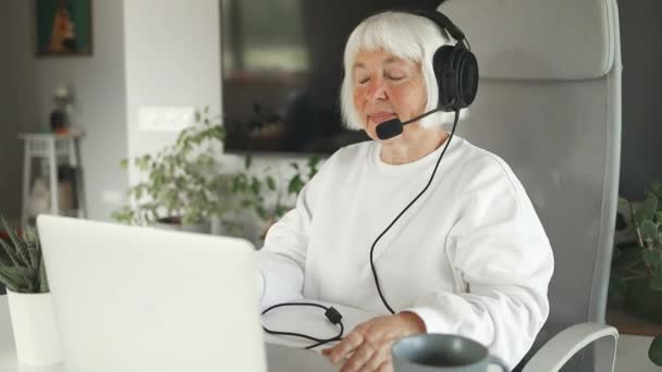 白种人漂亮的50多岁女人在家里的后视镜呼叫中心工作 有魅力的高级员工坐在桌子上 头戴耳机 用笔记本电脑聊天来支持工作场所的客户 — 图库视频影像